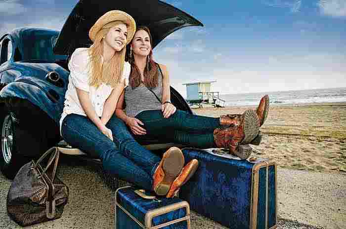 Två flickor sitter vid en bil vid stranden med sin packning, redo att åka på semester.